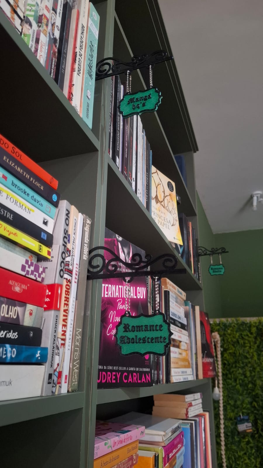 Placas pendentes identificando as seções da estante do Sebo Araxá, letreiro pintado à mão preso por correntes.